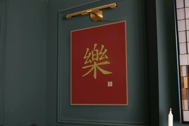 Joie à l'encre, laque rouge : affiche encadrée chêne sous une lampe de tableau, mur vert profond