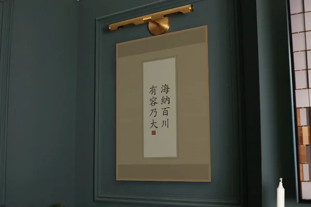 Qui sait accueillir devient grand en rouleau, sable ocre : affiche encadrée chêne sous une lampe de tableau, mur vert profond