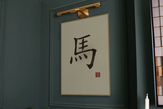 Signe du Cheval à l'encre, sable ocre : affiche encadrée chêne sous une lampe de tableau, mur vert profond